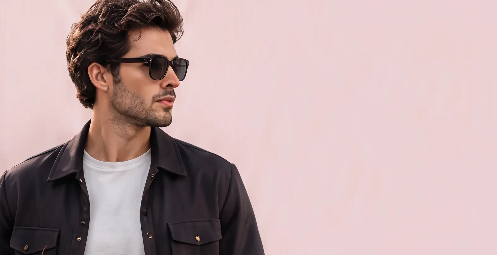 Man in dark overshirt and sunglasses against a pink wall